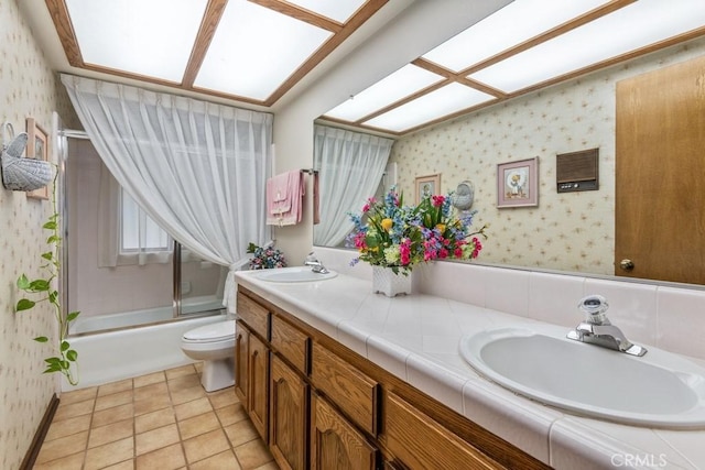 bathroom with double vanity, toilet, combined bath / shower with glass door, a sink, and wallpapered walls