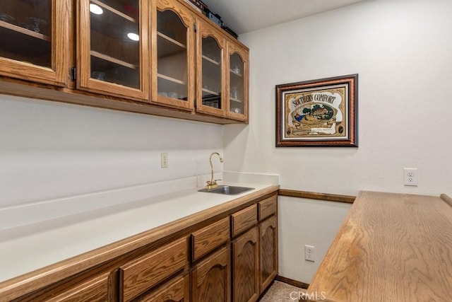 kitchen featuring light countertops, brown cabinetry, a sink, and glass insert cabinets