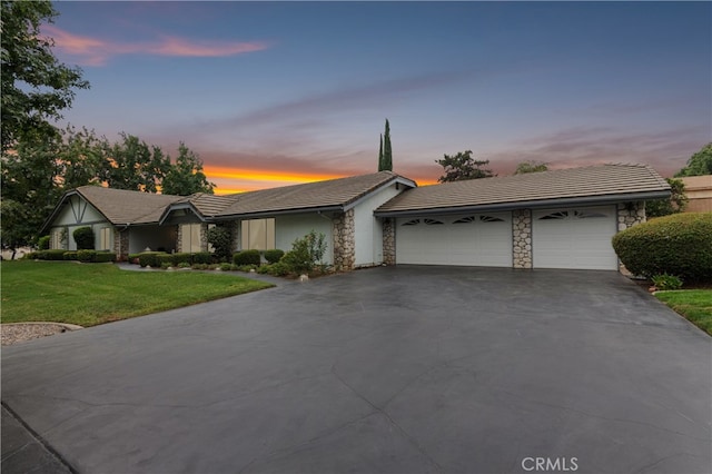 view of front of home with an attached garage, stone siding, driveway, and a yard