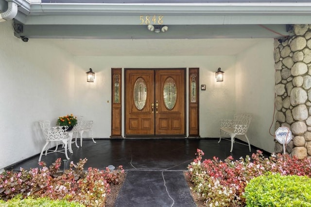 entrance to property with stone siding, covered porch, and stucco siding