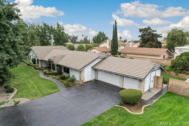 view of front of house featuring driveway, a garage, stone siding, fence, and a front yard