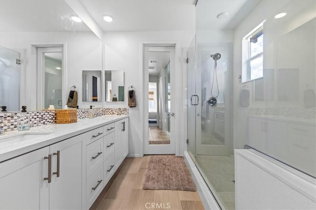 full bath with tasteful backsplash, double vanity, a shower stall, and wood finished floors