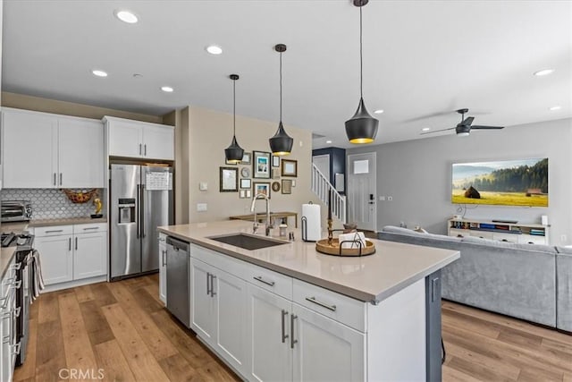 kitchen with light wood finished floors, appliances with stainless steel finishes, open floor plan, white cabinetry, and a sink