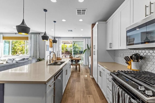 kitchen featuring stainless steel appliances, a sink, visible vents, open floor plan, and tasteful backsplash