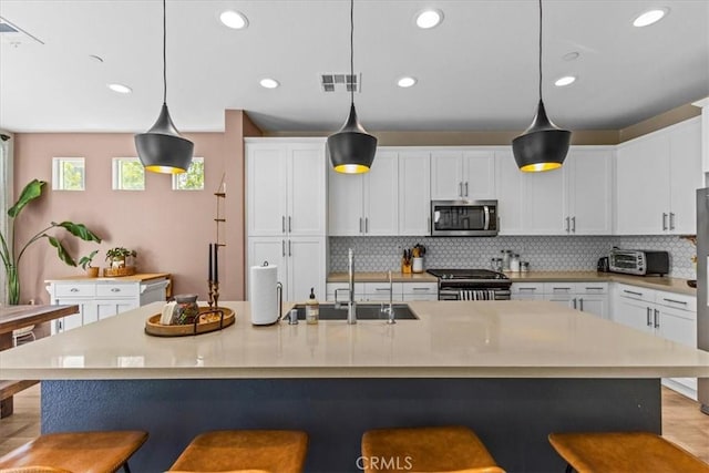 kitchen with visible vents, decorative backsplash, stainless steel appliances, a kitchen bar, and a sink