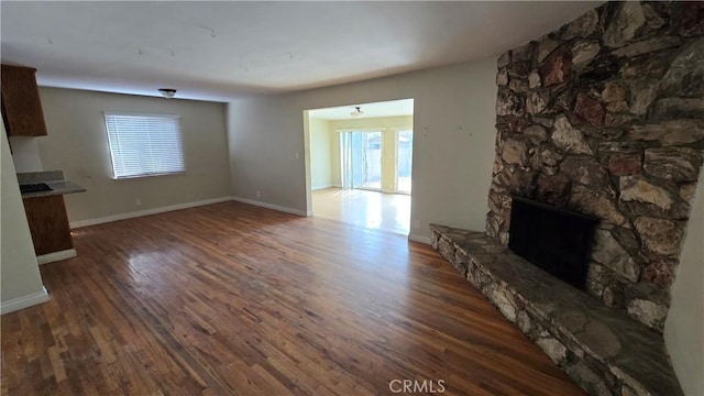 unfurnished living room with a wealth of natural light, baseboards, wood finished floors, and a stone fireplace