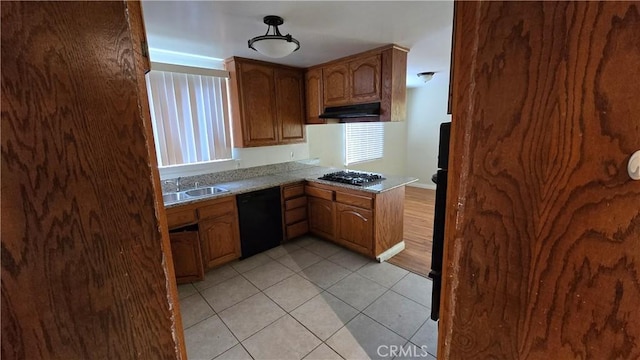 kitchen with light tile patterned floors, under cabinet range hood, a sink, gas stovetop, and black dishwasher