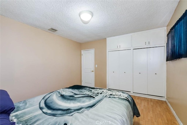 bedroom with a textured ceiling, visible vents, baseboards, a closet, and light wood finished floors