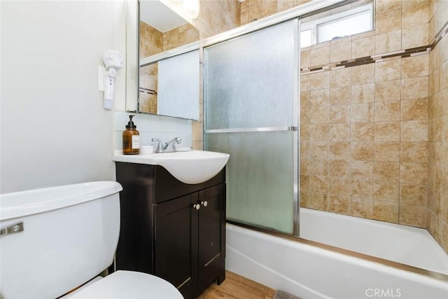 full bathroom with toilet, shower / bath combination with glass door, wood finished floors, and vanity