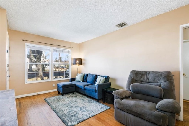 living room featuring a textured ceiling, hardwood / wood-style floors, visible vents, and baseboards