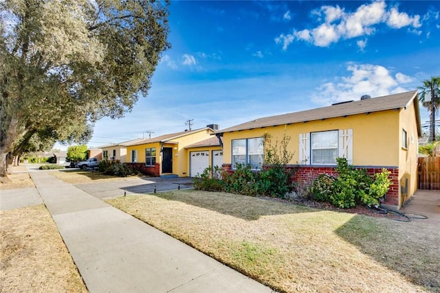 single story home featuring a garage, driveway, brick siding, a front yard, and stucco siding