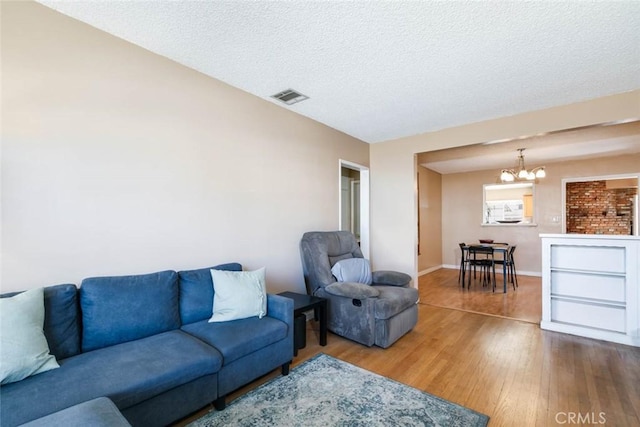 living room featuring visible vents, an inviting chandelier, a textured ceiling, wood finished floors, and baseboards