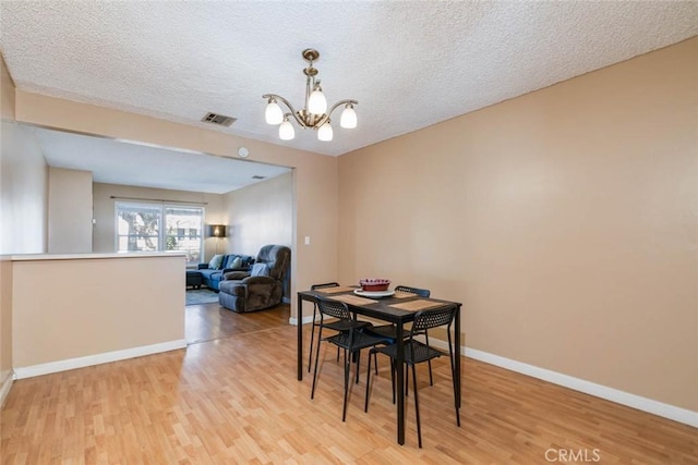 dining area featuring visible vents, baseboards, light wood-style flooring, a textured ceiling, and a chandelier