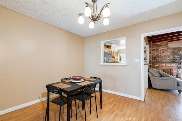 dining space with a chandelier, light wood finished floors, a textured ceiling, and baseboards