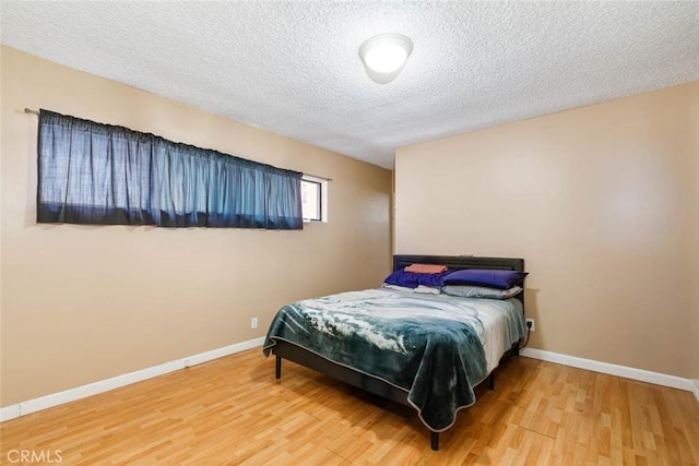 bedroom featuring a textured ceiling, baseboards, and wood finished floors