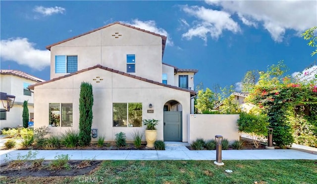 mediterranean / spanish house with a tile roof, stucco siding, a gate, fence, and a front lawn