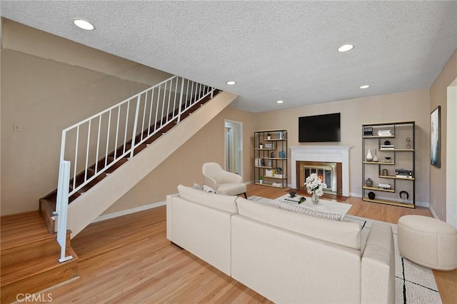 living area featuring a fireplace with flush hearth, stairway, wood finished floors, and a textured ceiling