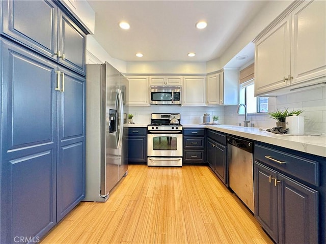 kitchen featuring white cabinets, light countertops, appliances with stainless steel finishes, light wood-type flooring, and backsplash