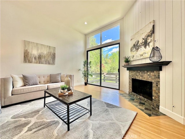 living area featuring a fireplace with flush hearth, baseboards, a high ceiling, and wood finished floors