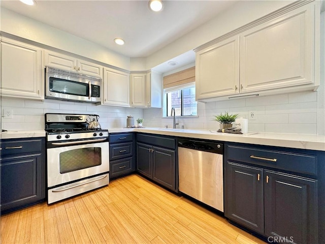 kitchen with light wood finished floors, appliances with stainless steel finishes, a sink, and decorative backsplash