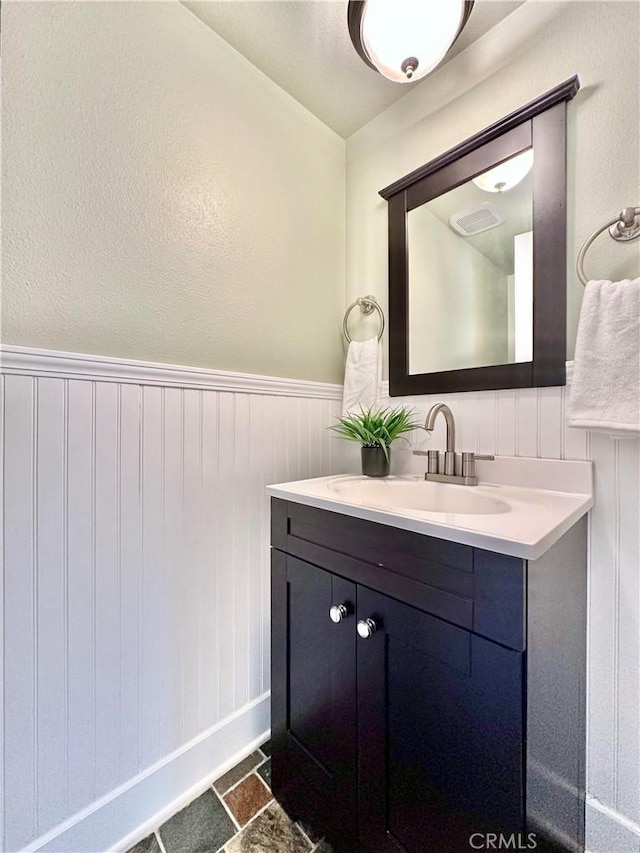 bathroom with visible vents, stone finish flooring, a wainscoted wall, and vanity