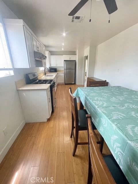 1238 W 35th St, Los Angeles, CA 90007 - kitchen featuring appliances with stainless steel finishes, under cabinet range hood, light countertops, a sink, and white cabinetry