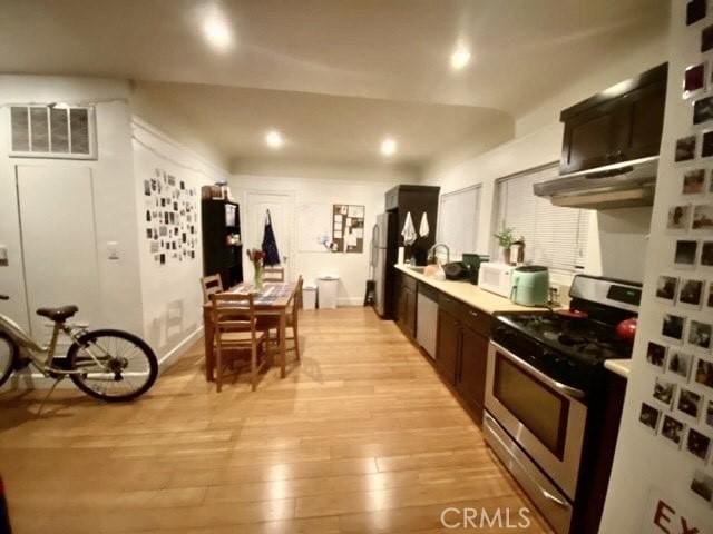 kitchen featuring visible vents, under cabinet range hood, white appliances, light wood-style floors, and light countertops