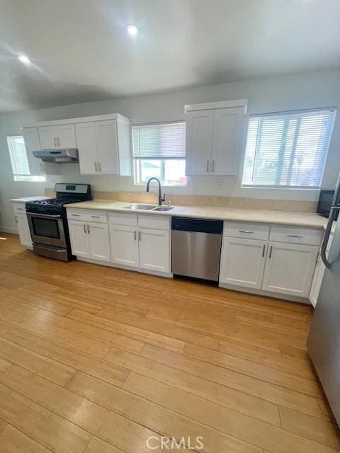 kitchen with light wood-type flooring, a sink, under cabinet range hood, stainless steel appliances, and white cabinets