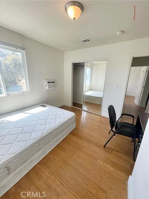 bedroom with visible vents, an AC wall unit, a closet, light wood finished floors, and baseboards