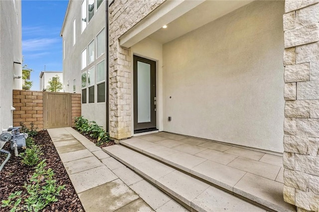 view of exterior entry featuring a patio, fence, stone siding, a gate, and stucco siding