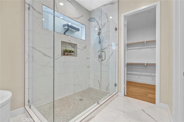 full bathroom featuring toilet, baseboards, marble finish floor, a stall shower, and a walk in closet