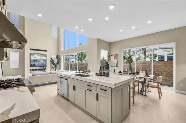 kitchen with open floor plan, light stone countertops, gray cabinetry, wall chimney range hood, and a sink