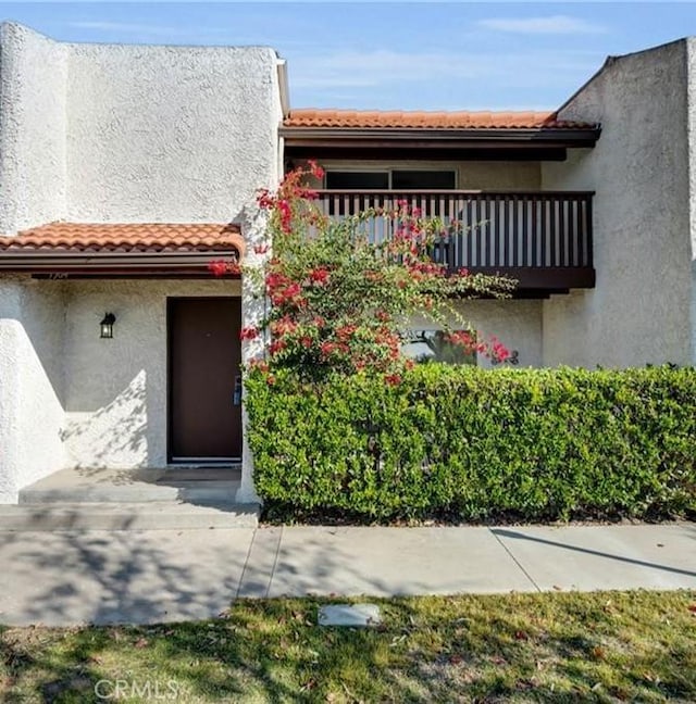 view of front of property featuring a tile roof, a balcony, and stucco siding