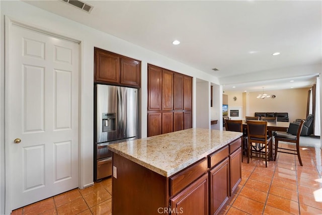 kitchen with visible vents, a kitchen island, light stone counters, open floor plan, and stainless steel refrigerator with ice dispenser