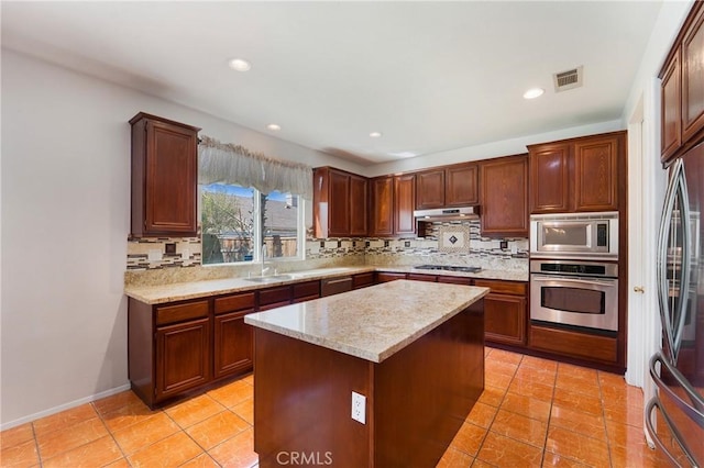 kitchen featuring under cabinet range hood, stainless steel appliances, a sink, visible vents, and backsplash