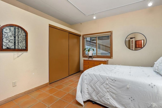 bedroom with track lighting, a closet, baseboards, and light tile patterned floors