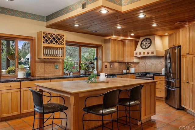 kitchen featuring stainless steel appliances, a kitchen island, wood counters, premium range hood, and a kitchen breakfast bar