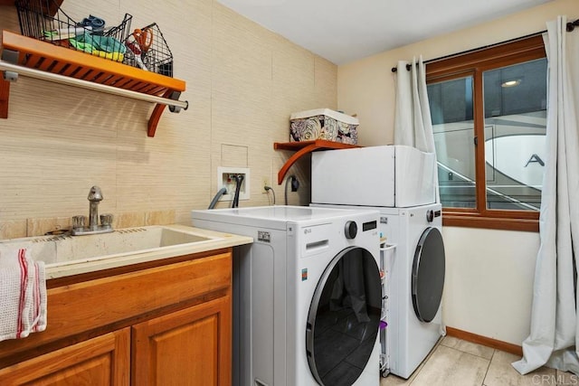 laundry area featuring light tile patterned floors, a sink, baseboards, cabinet space, and washer and clothes dryer