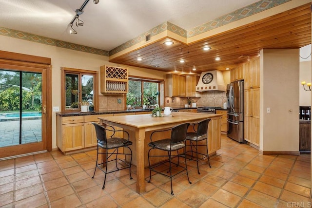 kitchen with a kitchen island, wooden counters, decorative backsplash, stainless steel fridge, and custom range hood