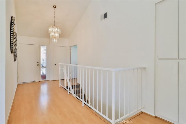 hall with a chandelier, light wood-type flooring, visible vents, and high vaulted ceiling