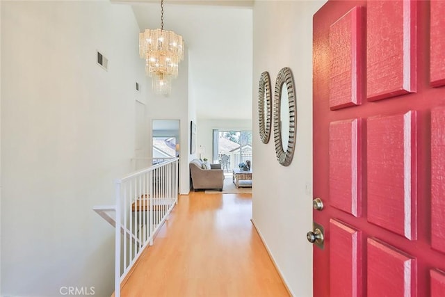 foyer entrance featuring light wood finished floors, a high ceiling, visible vents, and a chandelier