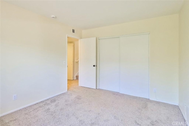 unfurnished bedroom featuring a closet, light colored carpet, visible vents, and baseboards