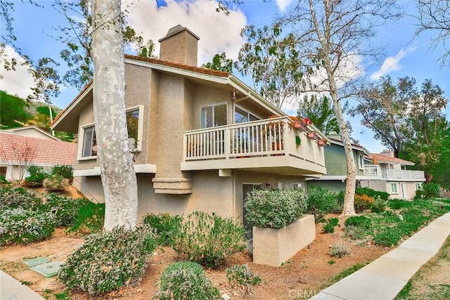 exterior space featuring a chimney, a balcony, and stucco siding