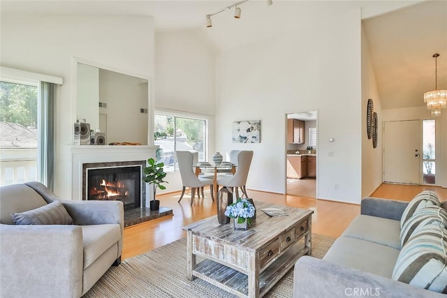 living room with light wood-type flooring, an inviting chandelier, high vaulted ceiling, and track lighting