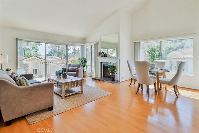 living area with high vaulted ceiling, a lit fireplace, and wood finished floors