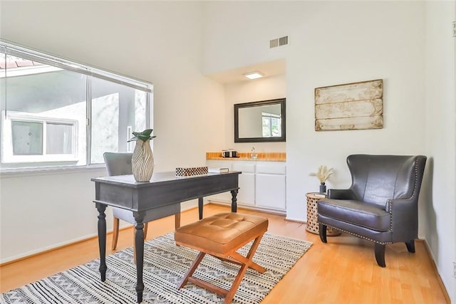 office space with a high ceiling, baseboards, visible vents, and light wood finished floors