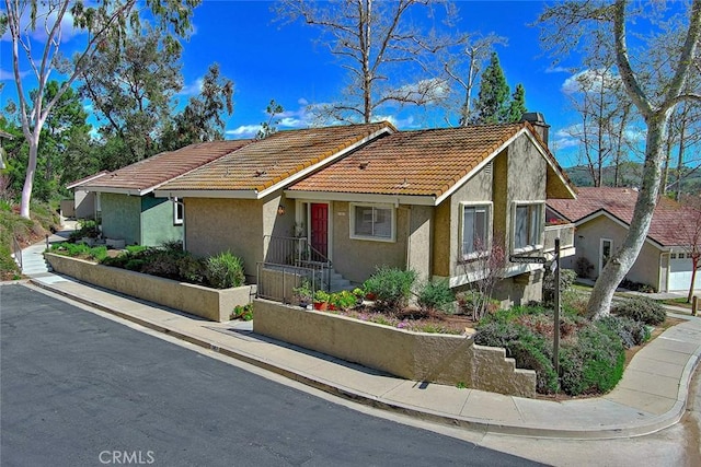 view of front of property featuring a tiled roof, a chimney, and stucco siding