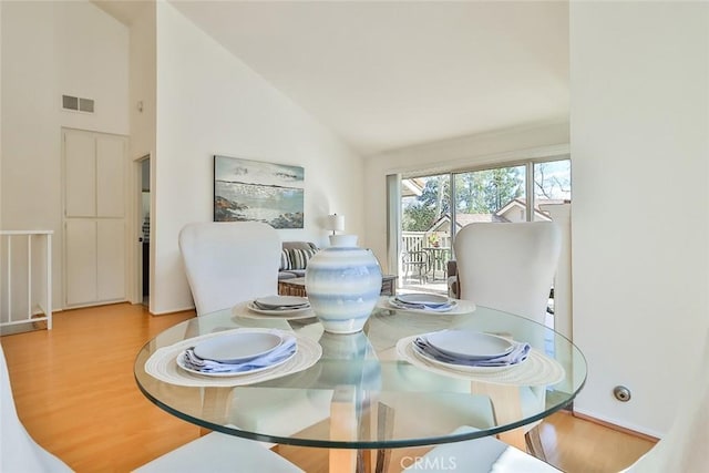 dining room featuring high vaulted ceiling, wood finished floors, and visible vents