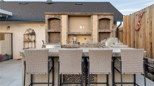 view of patio featuring exterior kitchen, outdoor wet bar, fence, and area for grilling