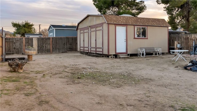 outdoor structure at dusk with a fenced backyard, a shed, and an outdoor structure